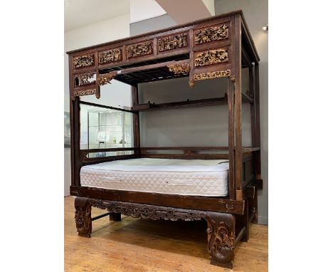 A Chinese parcel gilt opium or canopy bed, circa 1900, with latticed and panelled roof above seven carved panels depicting sc