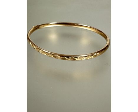 A 9ct gold stiff sprung bangle with half engraved diamond design and clip fastening to side no signs of damage or hard solder