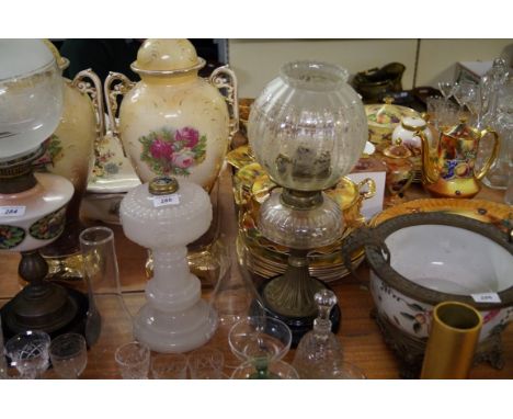A milk glass oil lamp (lacking fittings) together with a cut glass and brass oil lamp.