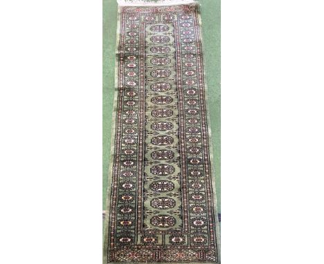 A green ground runner decorated with geometric patterns, 178cm long x 64cm width. Estimate £20-40.
