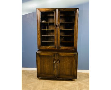 An Ercol two part display cabinet with a pair bevelled glass doors and five adjustable interior shelves to the top section, o