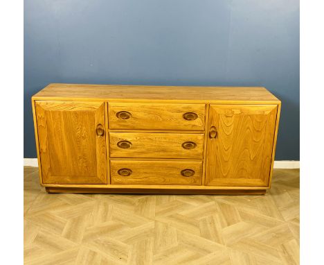 A blonde Ercol low level sideboard with a bank of three central drawers, the top drawer with a sliding cutlery tray, flanked 