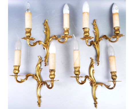 A set of four early 20th Century Rococo influence gilded metal wall light sconces fixtures. Each a twin sconce example with a