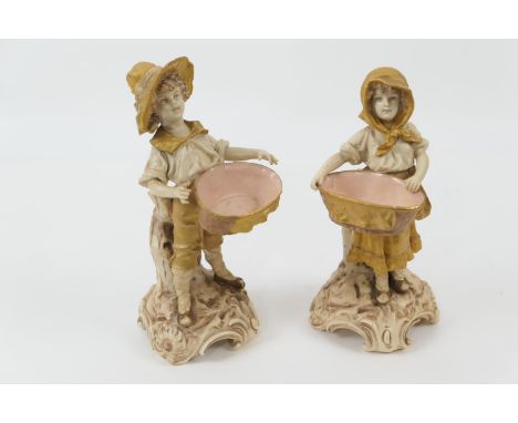 Pair of Austrian porcelain figural table salts, circa 1900, modelled as a boy and girl, each supporting a basket, decorated i