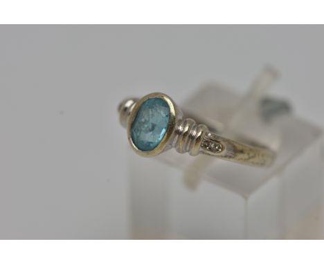 A WHITE METAL GEM SET RING, an oval cut topaz, bezel set, flanked with four round brilliant cut diamonds, stamped 9k, ring si