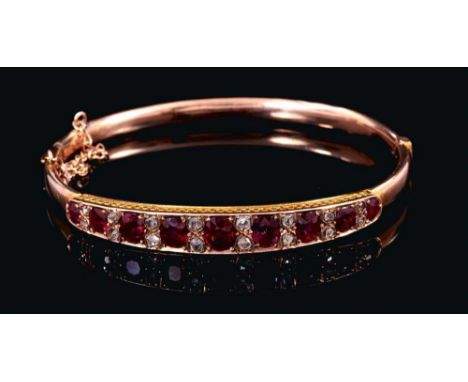 Late Victorian ruby and diamond hinged bangle with nine graduated oval mixed cut rubies interspaced by rose cut diamonds in g