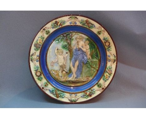 A 19th Century Majolica ceramic charger depicting a lady playing the flute a dancing faun having floral doors (a/f)