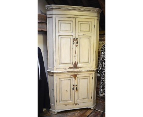 An antique painted pine cream two part standing corner cupboard, with two pairs of panelled doors enclosing blue painted shel