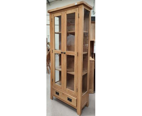 A modern light oak glazed double door cabinet with drawers below 181 x 60 x 32cm 