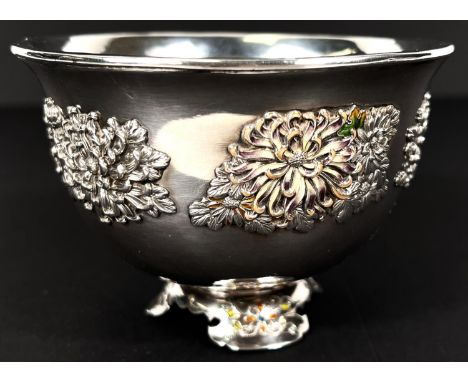 A Japanese white metal circular bowl decorated in relief and coloured enamels with chrysanthemum flowers, on trefoil raised f