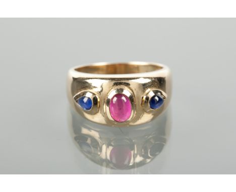 RUBY AND SAPPHIRE THREE STONE RING formed by a broad band set with a central oval cabochon ruby and flanked by two pear shape