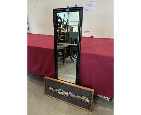 An ebonised long mirror and a framed woolwork
