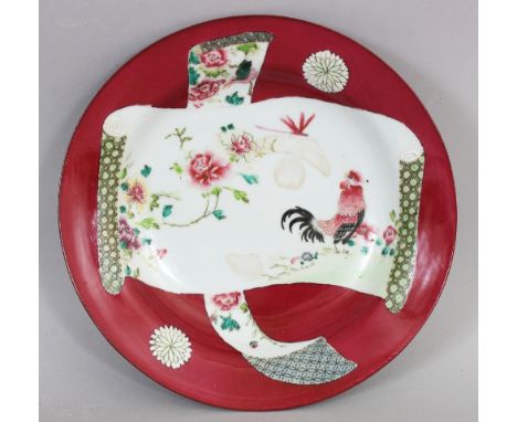 A GOOD QUALITY YONGZHENG STYLE FAMILLE ROSE RUBY GROUND PORCELAIN PLATE, decorated with a scroll-form panel of a cockerel and