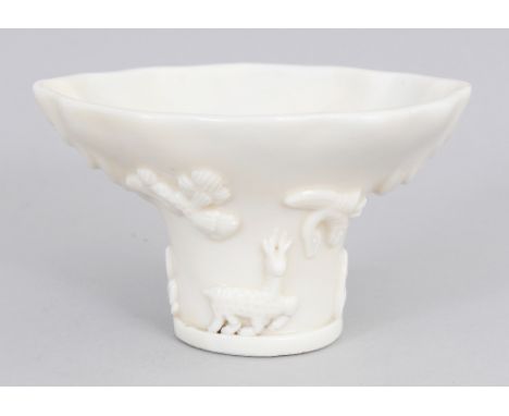 A CHINESE KANGXI PERIOD BLANC-DE-CHINE PORCELAIN LIBATION BOWL, the sides moulded in relief with a dragon, cloud scrolls, pin