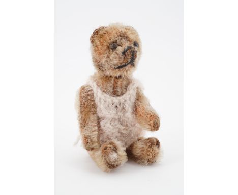 A 1930s miniature Teddy bear probably by Schuco, having articulated limbs, golden mohair, steel button eyes and a horizontall