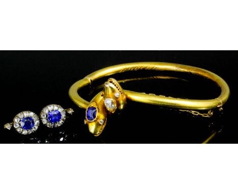 A late 19th Century gold coloured metal, sapphire and diamond set serpent head pattern stiff bangle, the intertwined serpents
