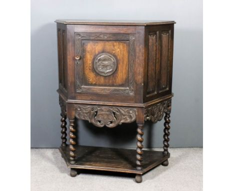 A panelled oak cabinet of "17th Century" design with angled front, fitted shelf enclosed by a panelled door with carving to c