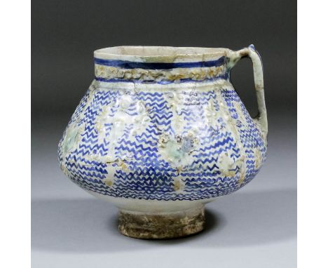 A Minai pottery jug of squat bi-conical form with vertical strap handle, the body moulded with bosses and medallions in low r