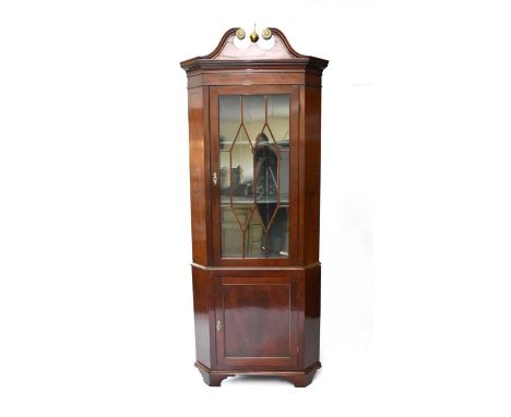 A 19th century mahogany veneered floor standing corner cupboard, the top with a broken swan-neck pediment with brass paterae,