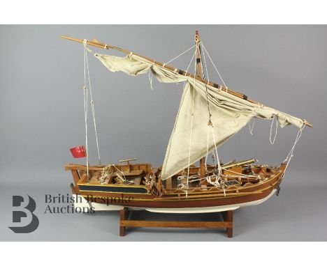 A large wooden sailboat model with single triangular sail, 10 oars and 3 cannons and cannonballs on a wooden stand. Boat meas