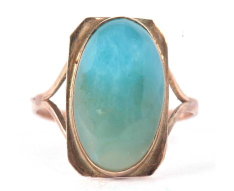 An Arts and Crafts style ring, the oval blue/turquoise cabochon, collet mounted with a rectangular plaque with chamfered corn