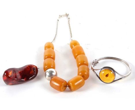 An amber nugget pendant, 7cm long, 33.7g, together with an unmarked white metal and amber hinged bangle, and a faux amber bea