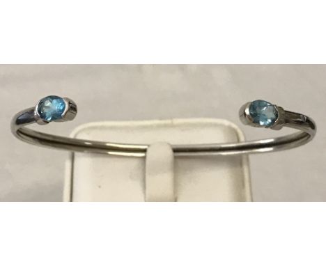 A 9ct white gold bangle set with 2 oval cut blue topaz stones.  Total weight 5.8g.