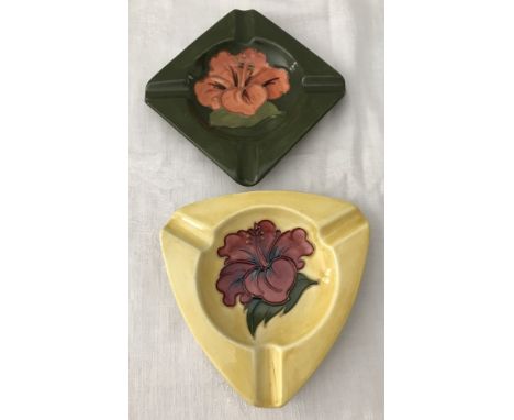 2 Moorcroft ceramic ashtrays. Triangular shape in yellow with red hibiscus flower to centre together with a square shape in g