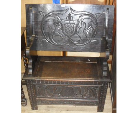 A mid to late 20th Century oak monks bench of small proportions, having carved decoration of a stylised shield with lion and 
