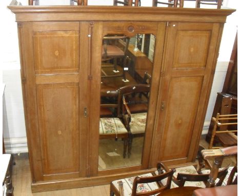 A good quality Arts & Crafts inlaid oak wardrobe, the central mirror flanked by two panelled cupboard doors enclosing hanging