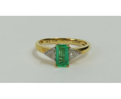 A contemporary 18ct gold emerald and diamond ring, the step cut emerald flanked by a triangular cut diamond on either side, f