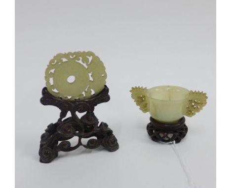 Chinese jade archaic style cup with carved handles and pierced wooden stand, with small rim chip and internal crack, 9cm wide