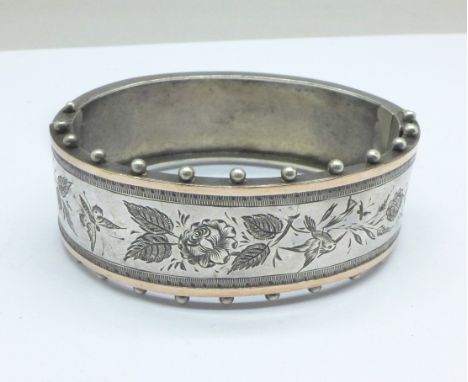 A Victorian sterling silver bangle decorated with birds and flowers, banded with gold, 24g