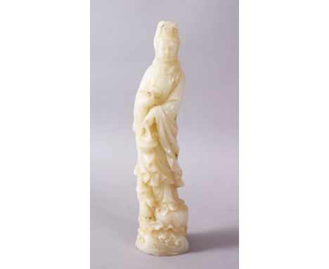 A CHINESE CARVED WHITE JADE FIGURE OF GUANYIN, stood upon a rocky outcrop holding a floral basket 21cm high