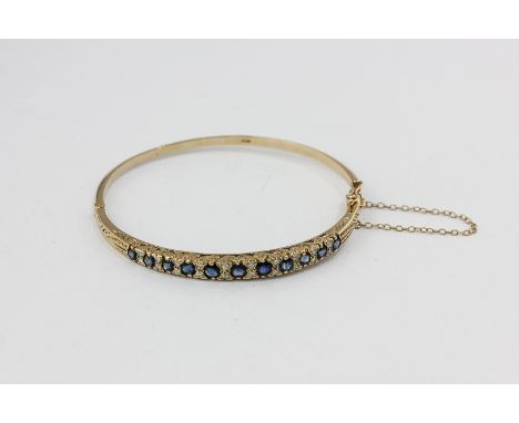 A sapphire and diamond hinged bangle set with eleven graduated round sapphires with pairs of diamonds between, in 9ct gold