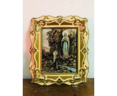 A Religious picture in a cream and gilt frame with a light behind.
