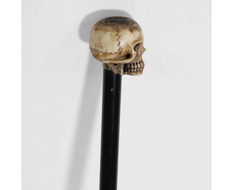An ebonised swagger stick, early 20th century, the slender shaft surmounted by a carved bone finial modelled as a skull, 91cm