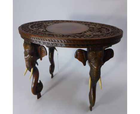 An Indian teak occasional low table with carved decoration to the oval top and raised on carved elephant head legs, H 48 x W 