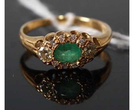 An 18ct gold, emerald and diamond cluster ring, the claw set oval cut emerald in a surround of round cut diamonds, 2.6g, size