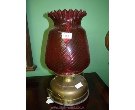 An unusual Church oil heater/lamp with two handled brass base standing on three feet, cranberry glass globe shade with swirl 