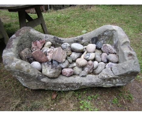 A weathered natural stone trough of rectangular form with single curved end containing a quantity of various pebbles, etc, 70