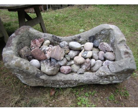 A weathered natural stone trough of rectangular form with single curved end containing a quantity of various pebbles, etc, 70