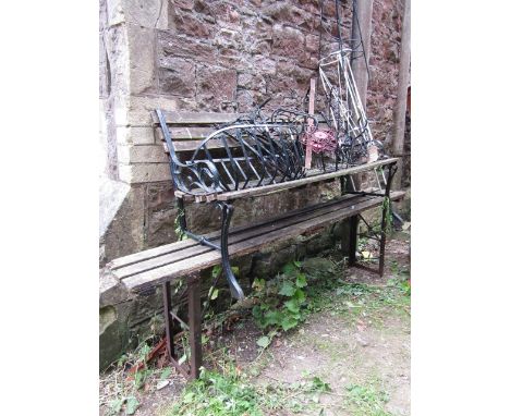 A small two seat garden bench with weathered wooden slatted seat and back raised on a pair of cast metal end supports togethe