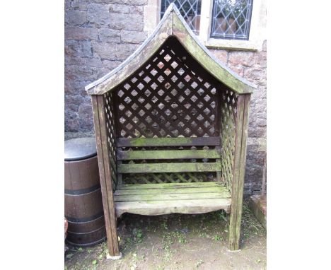 A stained and weathered pine framed arbour with open slatted bench seat and back within a lattice work panelled frame beneath