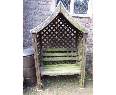 A stained and weathered pine framed arbour with open slatted bench seat and back within a lattice work panelled frame beneath