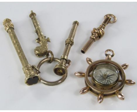 A yellow metal compass charm in the form of a ships wheel, together with a yellow metal watch key and three propelling pencil