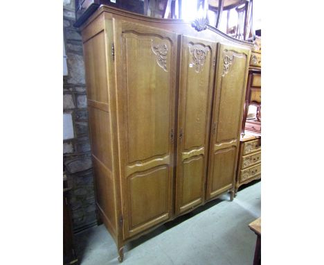 A pale oak three door wardrobe with carved and panelled detail raised on swept supports, 150 cm wide together with a matching