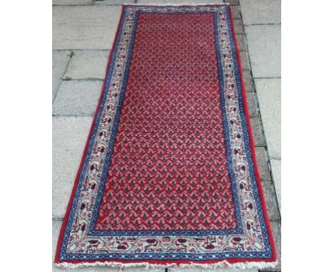A Persian runner, with geometric motifs on a red ground, within a multi border, 197 x 72 cm