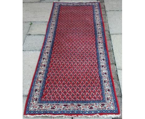 A Persian runner, with geometric motifs on a red ground, within a multi border, 197 x 72 cm