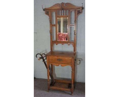 An Edwardian oak hall stand, circa 1910, with a shaped mirror set back with seven hat hooks, over a single drawer with flanki